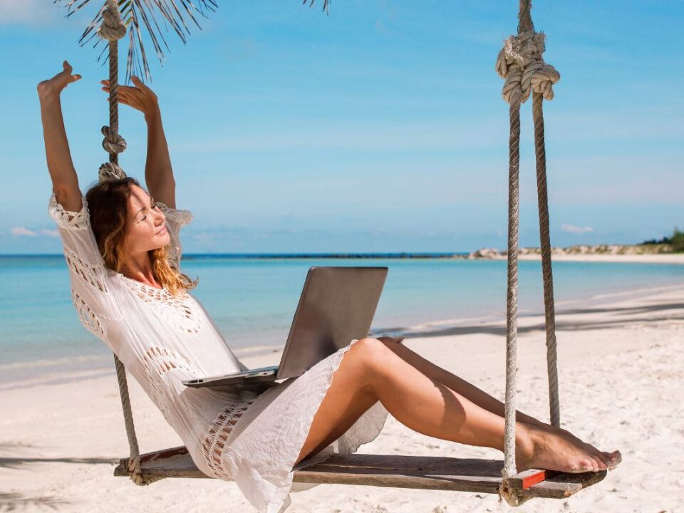 praca zdalna, może być wykonywana nawet na plaży, jak robi to dziewczyna zw zdjęcia, która siedzi na huśtawce, a na kolanach trzyma laptop.